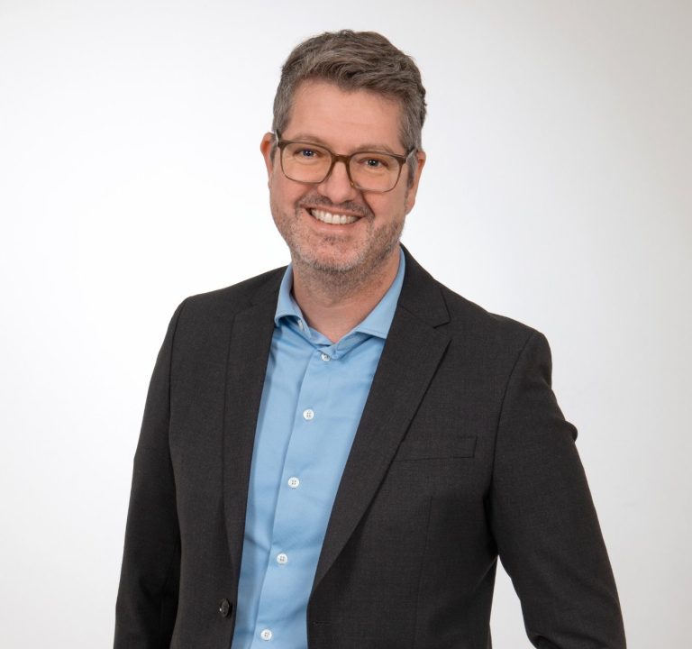 Rechtsanwalt Dr. Michael Bräuer Mann in Anzug mit Brille, lächelnd vor neutralem Hintergrund.